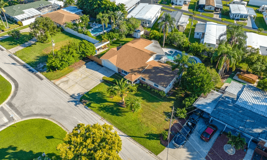 Aerial view of a single-family Florida home with a screened pool, driveway and mature palms in a suburban neighborhood