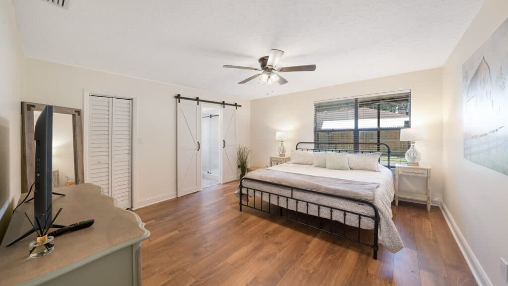 Bedroom with a wrought iron bed frame, barn door to the ensuite and wood-look flooring, captured for a 3D property tour