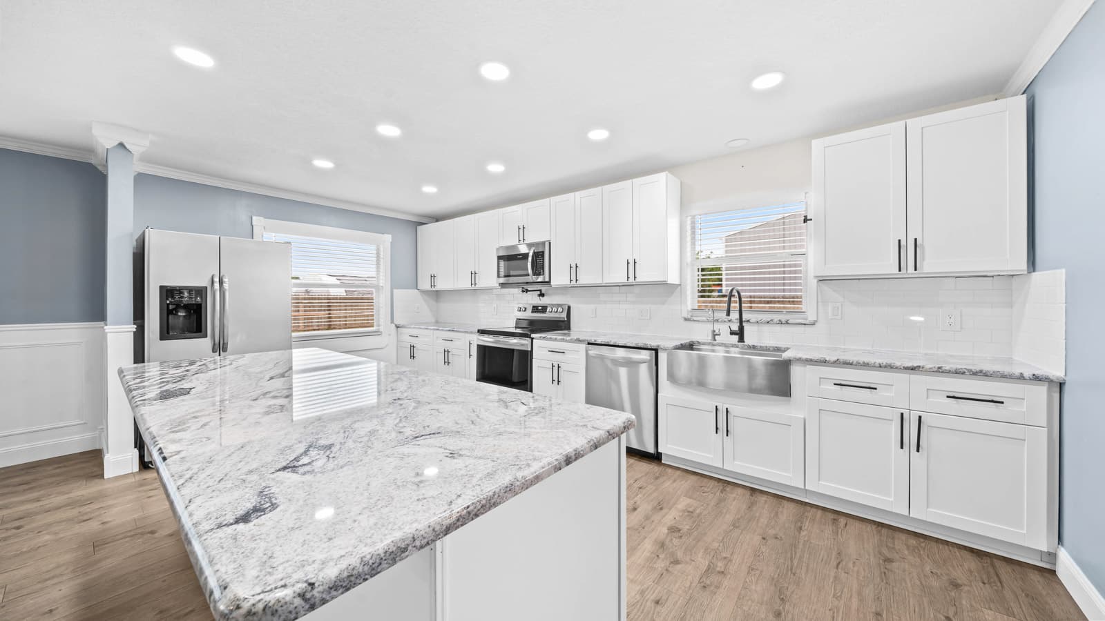 Open kitchen with a large granite island, white shaker cabinets and stainless appliances, photographed for a real estate listing