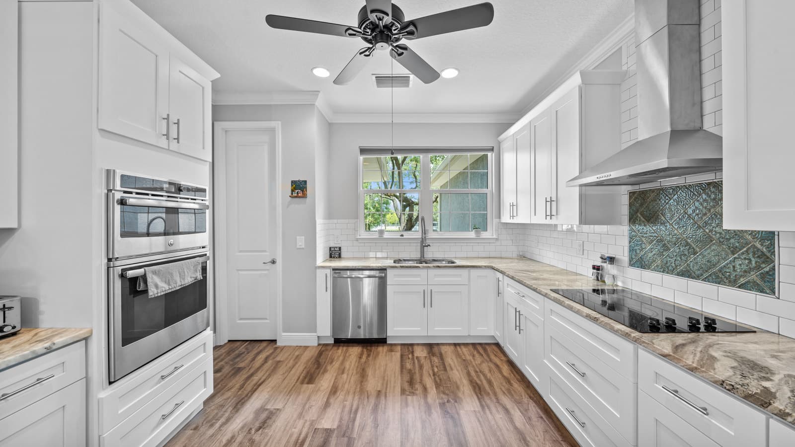 Bright white kitchen with subway tile backsplash, stainless range hood and wood-look flooring, filmed for a property video walkthrough